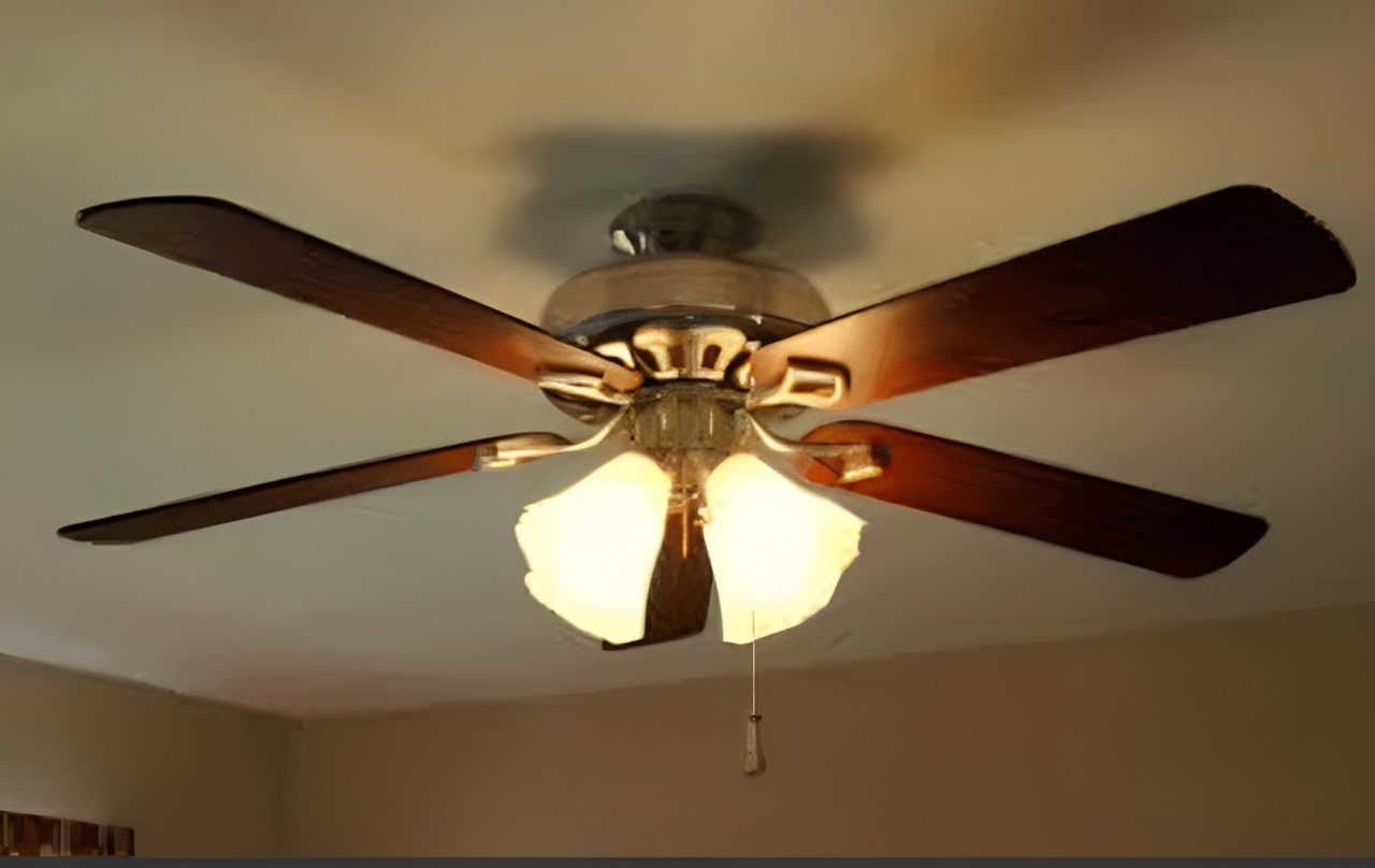 Ceiling fan with five wooden blades and four lights, mounted on a white ceiling.