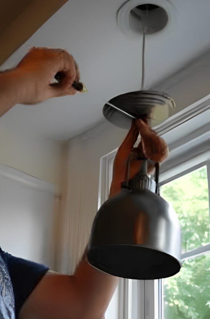 Person installing a ceiling light fixture, connecting wires safely.