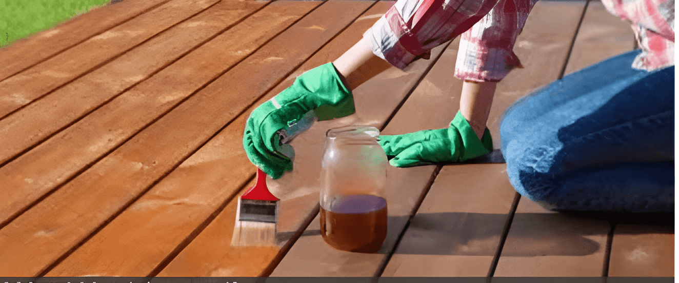 Person applying wood stain to a deck with a paintbrush.