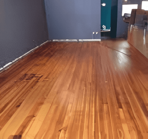 Hardwood floor half sanded and restored, showing the before and after.